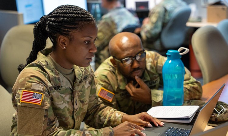 U.S. Army Lt. Briana Harvey, team lead for CPT 169 during CYBER FLAG 22, assists another soldier with a computer issue at the Laurel Readiness Center, Laurel, MD during CYBER FLAG 22 on Jul. 25, 2022. Cyber Flag 22 is an annual U.S. Cyber Command training event that is designed to strengthen partnerships, improve the defensive skills, and enhance the readiness and collaboration of the participating cyber operators. (U.S. Army National Guard photo by Sgt. Tom Lamb)