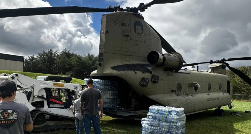 Soldiers unload crates of water in front of a CH-47 Chinook. On the side of it the face of singer Lionel Richie is stenciled on.