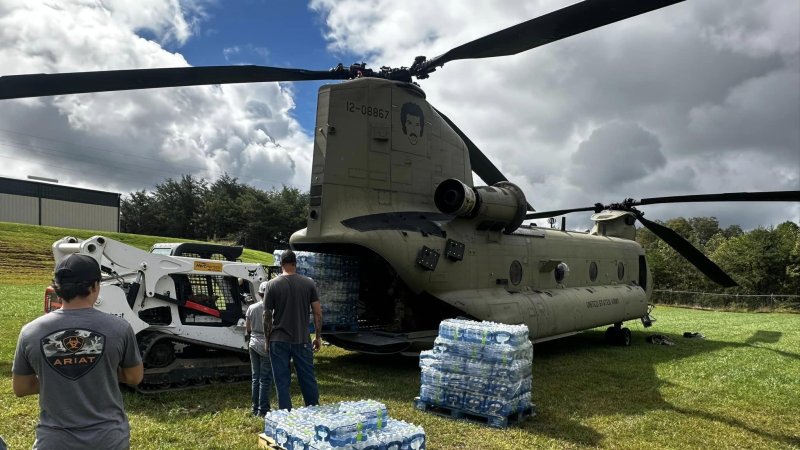 Soldiers unload crates of water in front of a CH-47 Chinook. On the side of it the face of singer Lionel Richie is stenciled on.