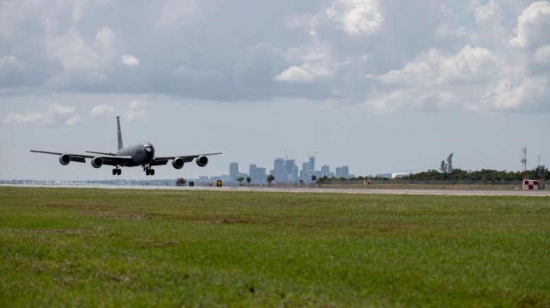 A KC-135 Stratotanker lands on a runway on a large field at MacDill Air Force Base, a city skyline behind it.