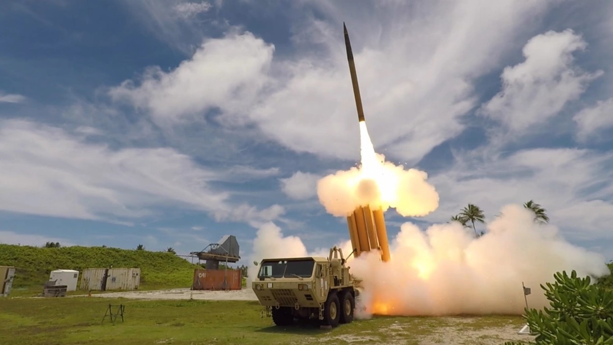 A THAAD rocket battery fires, with one munition launching from the system in a plume of fire into the sky.