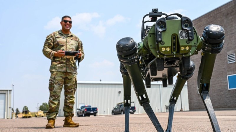 A man in uniform stands behind a four-legged robot.