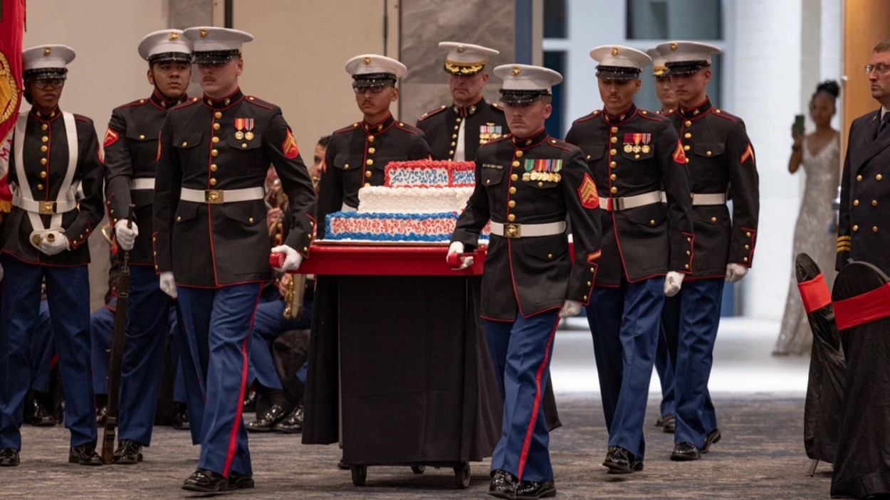 Marines in dress uniforms carry a large birthday cake.