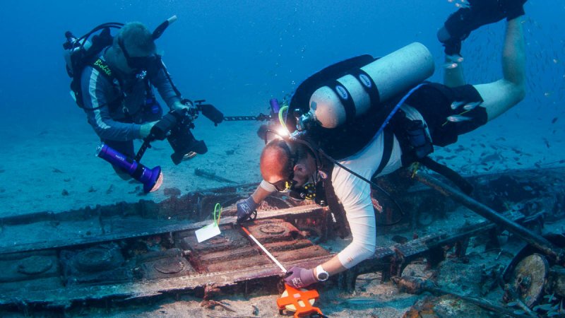 Archaeologists use measuring tapes and underwater cameras to record and document a WWII aircraft site in Papua New Guinea. Photo: Project Recover — Project Recover is a collaborative effort to enlist 21st-century science and technology in a quest to find and repatriate World War II MIAs to bring recognition to the service member, closure for their families, and to help a grateful Nation keep its sacred promise to bring our MIAs home. As a result of Project Recover’s missions, there are 84 MIAs awaiting recovery at this time (January 2020). Since 1993, Project Recover (formerly The BentProp Project) has located 30+ downed World War II US aircraft associated with scores of MIA service members.