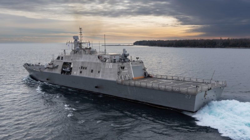 The littoral combat ship USS Nantucket sails on the water, the sun setting behind it.