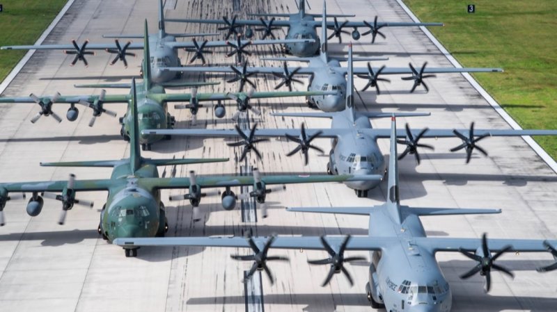 Seven C-130 aircraft are lined up along a runway.