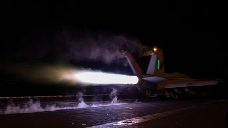 An F/A-18F Super Hornet takes off at night, with a bright exhaust.