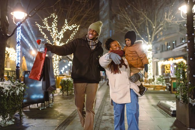 A happy family enjoying a festive evening walk with holiday lights and shopping bags.