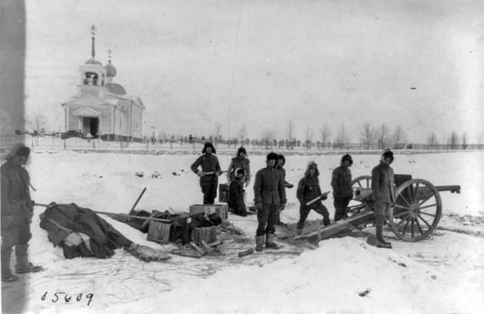 Black and white photo showing several American soldiers in the snow, a church behind them.