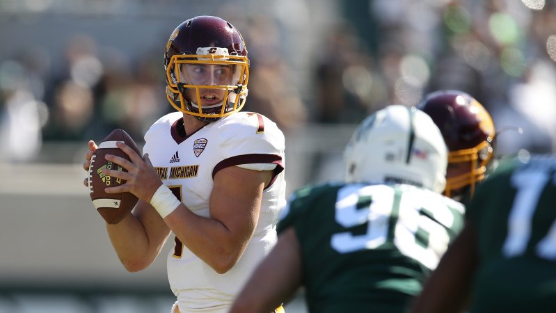 A football player holding the ball pulls back as defense rushes him.