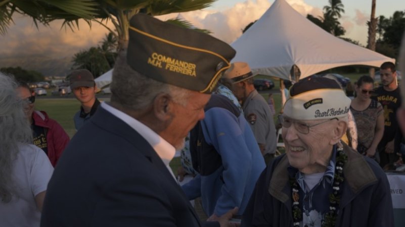 An older man shakes hands with a man in military uniform.