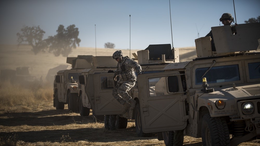 A soldier jumps out of a Humvee in a desert location.