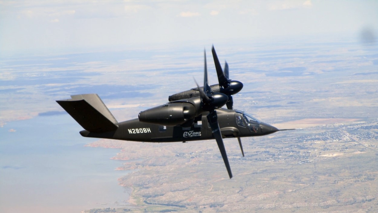 A tiltrotor aircraft flies across the plains.