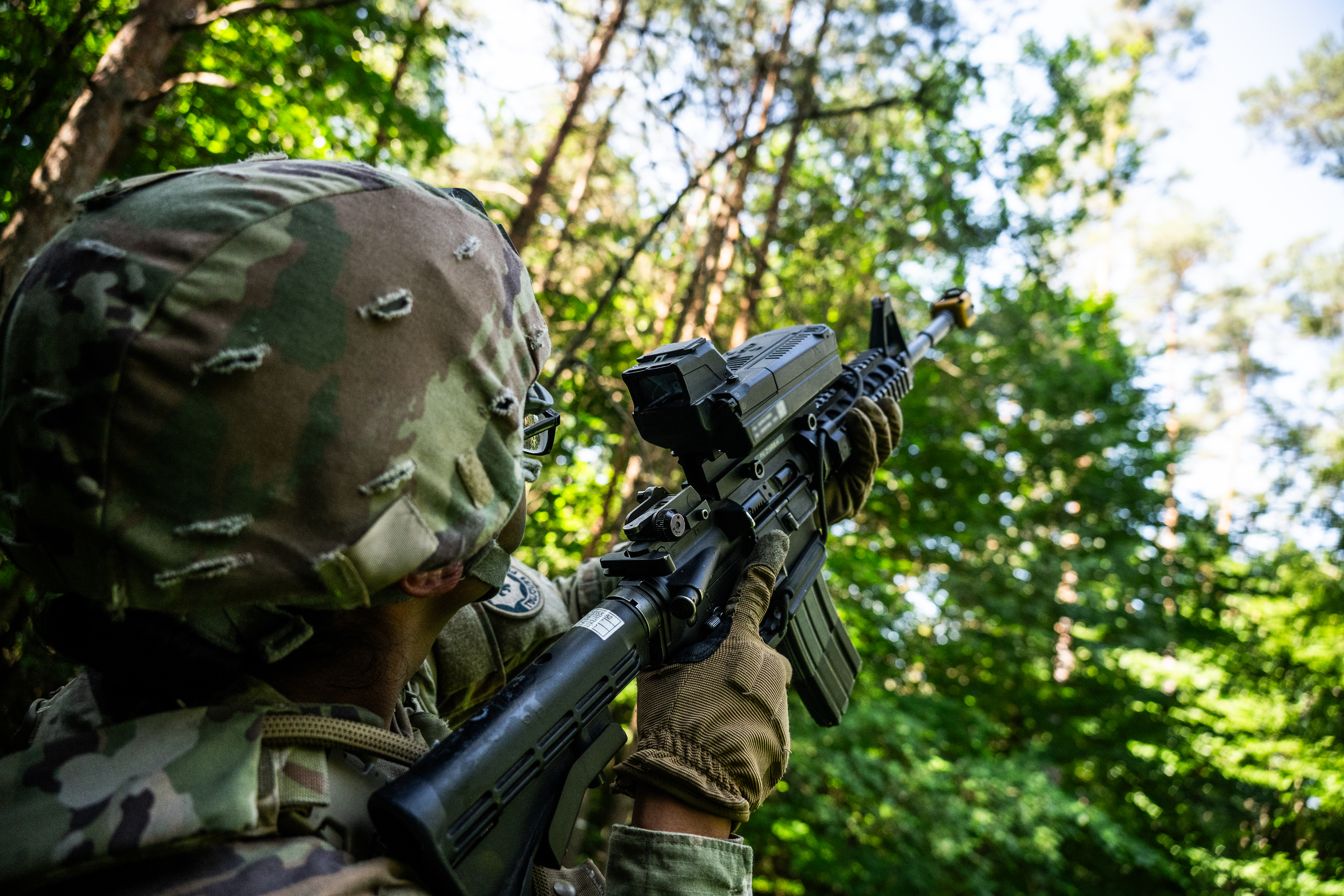 A U.S. Soldier assigned to 3rd Squadron, 2nd Cavalry Regiment pulls security using a SMASH 2000L attached to an M4A1 carbine rifle during Project Flytrap at Joint Multinational Readiness Center, Hohenfels Training Area, Hohenfels, Germany, June 20, 2025. The attachment provides the weapon operator with unmanned aerial system lock-on functionalities that fire automatically at its targets. (This photo has been blurred for operational security purposes) (U.S. Army photo by Spc. Elijah Magaña)
