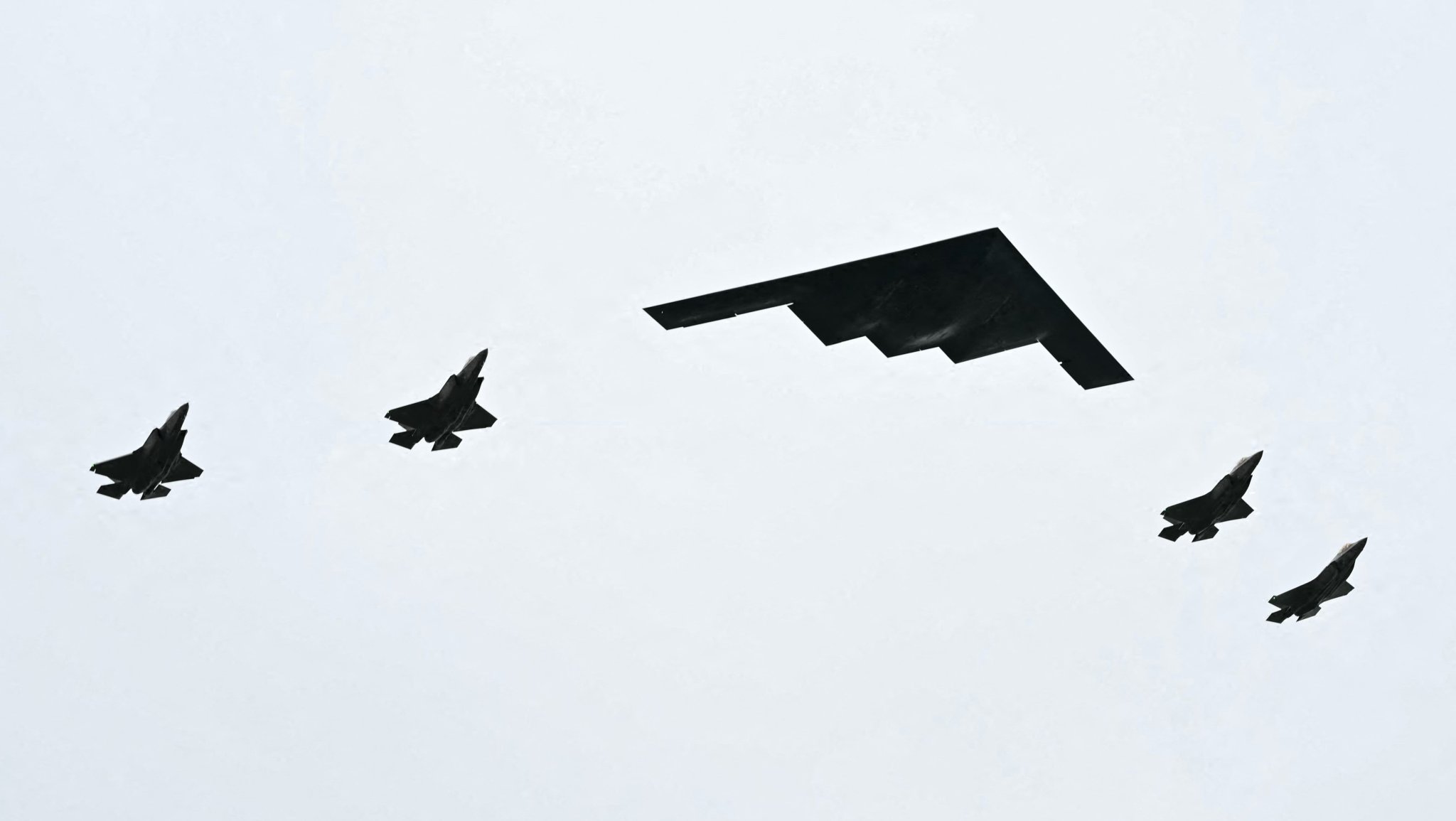 A B-2 bomber (C) and four F-35 fighter jets fly overhead as US President Donald Trump greets Russian President Vladimir Putin on the tarmac after they arrived at Joint Base Elmendorf-Richardson in Anchorage, Alaska, on August 15, 2025. Putin is in Alaska at the invitation of Trump in his first visit to a Western country since he ordered the 2022 invasion of Ukraine that has killed tens of thousands of people. (Photo by ANDREW CABALLERO-REYNOLDS / AFP) (Photo by ANDREW CABALLERO-REYNOLDS/AFP via Getty Images)