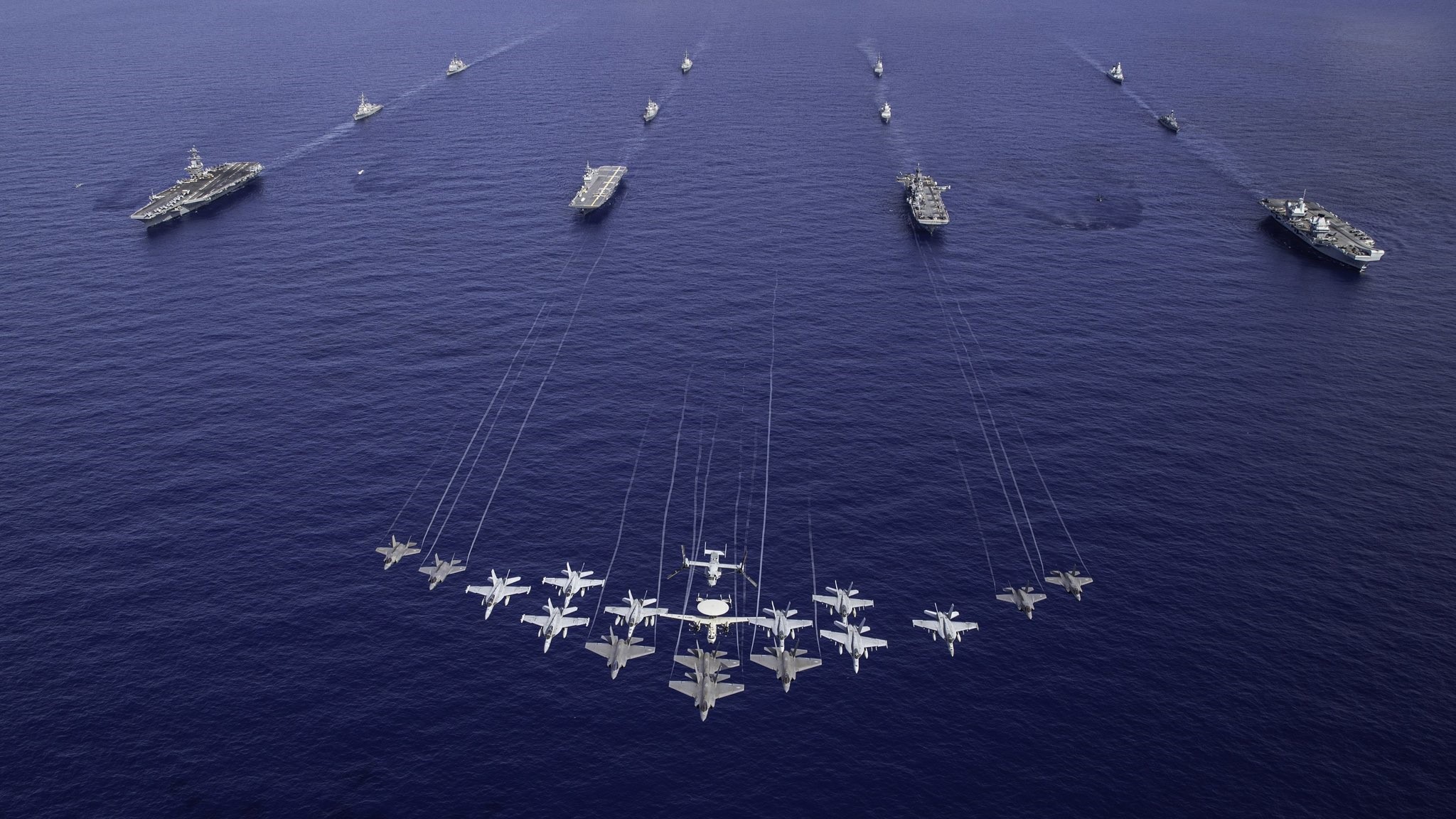USS George Washington (CVN-73), HMS Prince of Wales (R09), JS Kaga (DDH-184), and an American amphibious assault ship sail together in the North Philippine Sea, with several aircraft overhead.