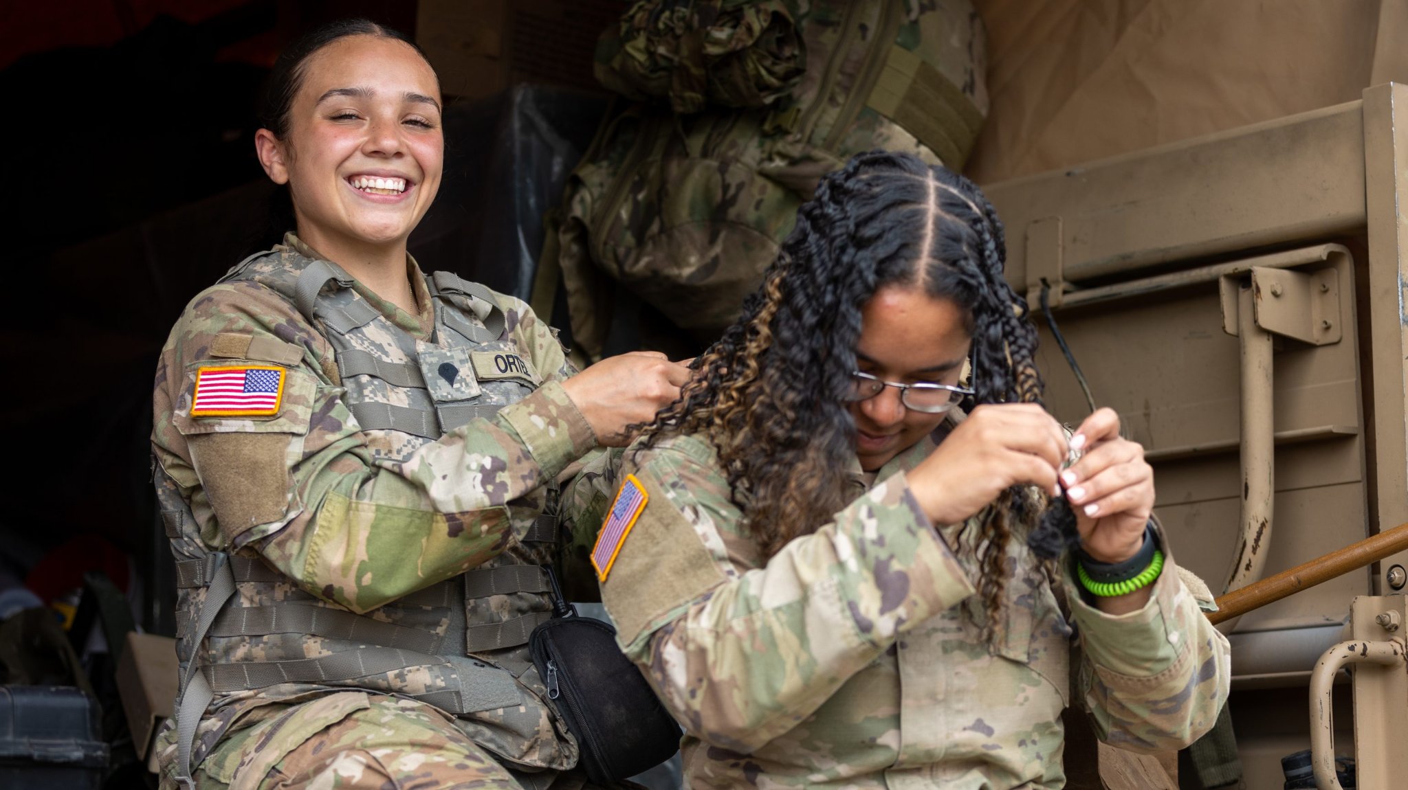 Specialist Rosealina Ortiz (left) assists Specialist Oscarina Pepen (right) with her hair following live fire training. CFB Gagetown, New Brunswick, Canada, August 9, 2022. In 2021 the Army released updated female grooming standards which are more inclusive of various natural hair styles. (U.S. Army National Guard photo by Spc. David Connors)