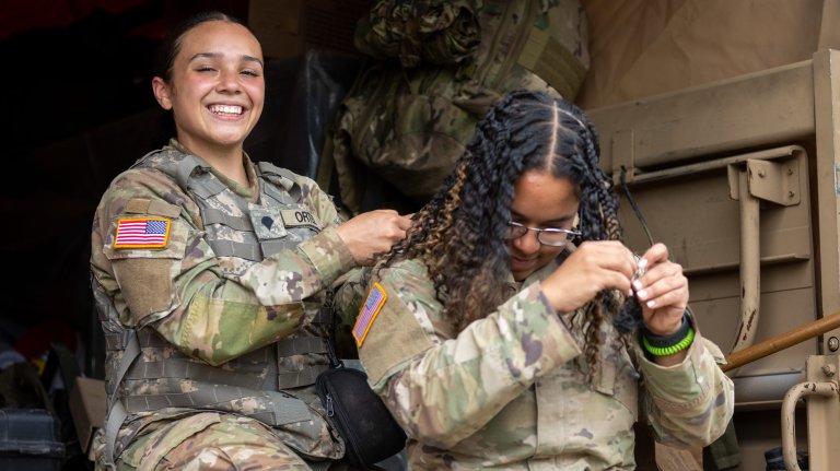 Specialist Rosealina Ortiz (left) assists Specialist Oscarina Pepen (right) with her hair following live fire training. CFB Gagetown, New Brunswick, Canada, August 9, 2022. In 2021 the Army released updated female grooming standards which are more inclusive of various natural hair styles. (U.S. Army National Guard photo by Spc. David Connors)