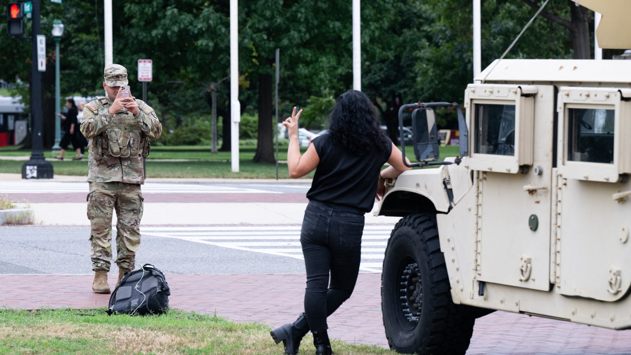 A member of the National Guard takes a photograph of a woman standing against military equipment as the National Guard patrols outside of Union Station in Washington, DC, August 21, 2025. President Donald Trump said he plans to patrol Washington's streets on Thursday with troops he deployed to the US capital in a show of force against what he claims is a "crime emergency." Trump ordered hundreds of National Guard to deploy in Washington last week vowing to "take our capital back," despite protests by some residents and statistics showing violent offenses falling. (Photo by SAUL LOEB / AFP)