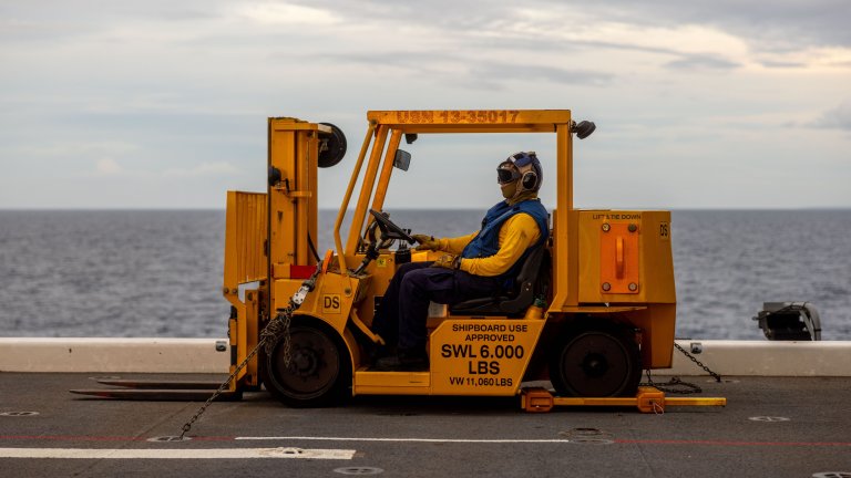 U.S. Navy Petty Officer Third Class Ivan Melendez, an aviation boatswain mate, sits in a forklift awaiting arrival of MV-22B Ospreys assigned to Marine Medium Tiltrotor Squadron (VMM) 363, Marine Rotational Force – Darwin 25.3, aboard the expeditionary sea base USS Miguel Keith (ESB 5) in the Philippine Sea, Aug. 29, 2025. For the first time in the rotation’s history, the MRF-D Marine Air-Ground Task Force's Aviation and Ground Combat Elements embarked aboard a U.S. Navy vessel to extend operational reach and provide flexible, combat-credible options across the Indo-Pacific. MRF-D is an annual six-month rotational deployment to enhance interoperability with the Australian Defence Force and allies and partners and provide a forward postured crisis response force in the Indo-Pacific. Melendez is a native of California. (U.S. Marine Corps photo by Cpl. Angelina Sara)