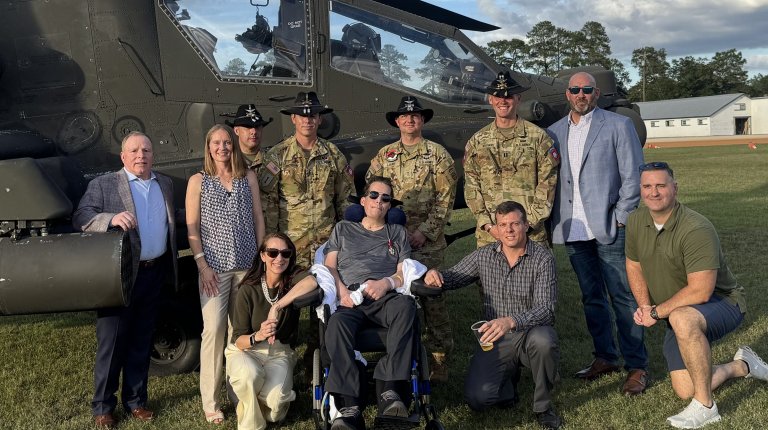 Garrett Illerbrunn, center, and Lorna Illerbrun, kneeling, surrounded by friends and pilots from their former units at Garrett's retirement ceremony in early October. Garrett was severly wounded in a 2023 drone attack in Iraq.