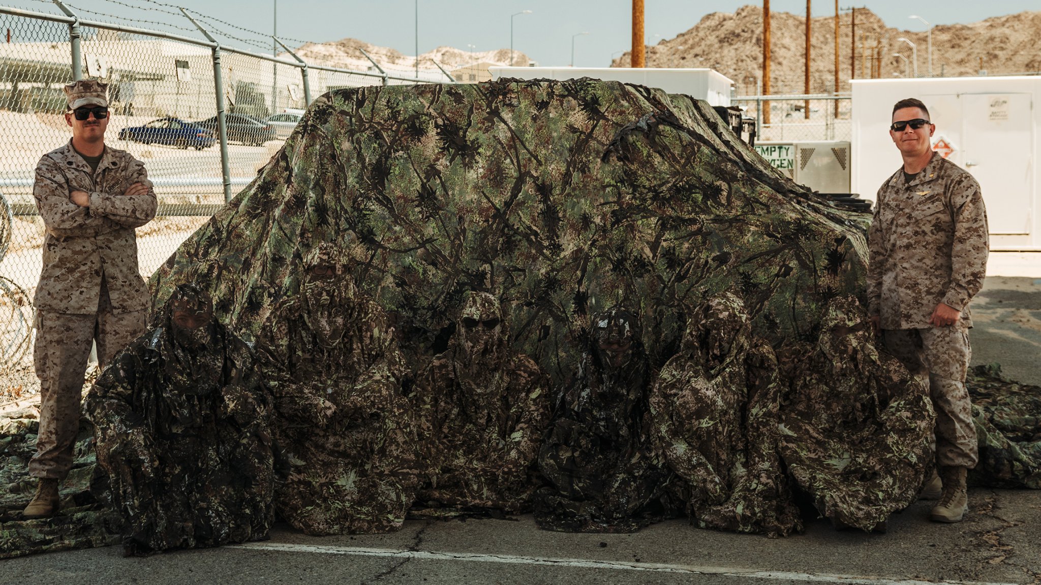 Walter Ising, left, and U.S. Marines with Tactical Training and Exercise Control Group, Marine Air Ground Task Force Training Command, Marine Corps Air Ground Combat Center pose for a photo with camouflage gear designed to enhance realism and effectiveness during Service Level Training Exercise 4-25 at MCAGCC, Twentynine Palms, California, July 21, 2025. SLTE provides integrated training across the Marine Air Ground Task Force to improve combat readiness and lethality. (U.S. Marine Corps photo by Lance Cpl. Micah Thompson)