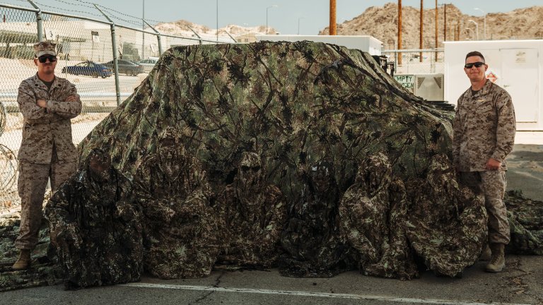 Walter Ising, left, and U.S. Marines with Tactical Training and Exercise Control Group, Marine Air Ground Task Force Training Command, Marine Corps Air Ground Combat Center pose for a photo with camouflage gear designed to enhance realism and effectiveness during Service Level Training Exercise 4-25 at MCAGCC, Twentynine Palms, California, July 21, 2025. SLTE provides integrated training across the Marine Air Ground Task Force to improve combat readiness and lethality. (U.S. Marine Corps photo by Lance Cpl. Micah Thompson)