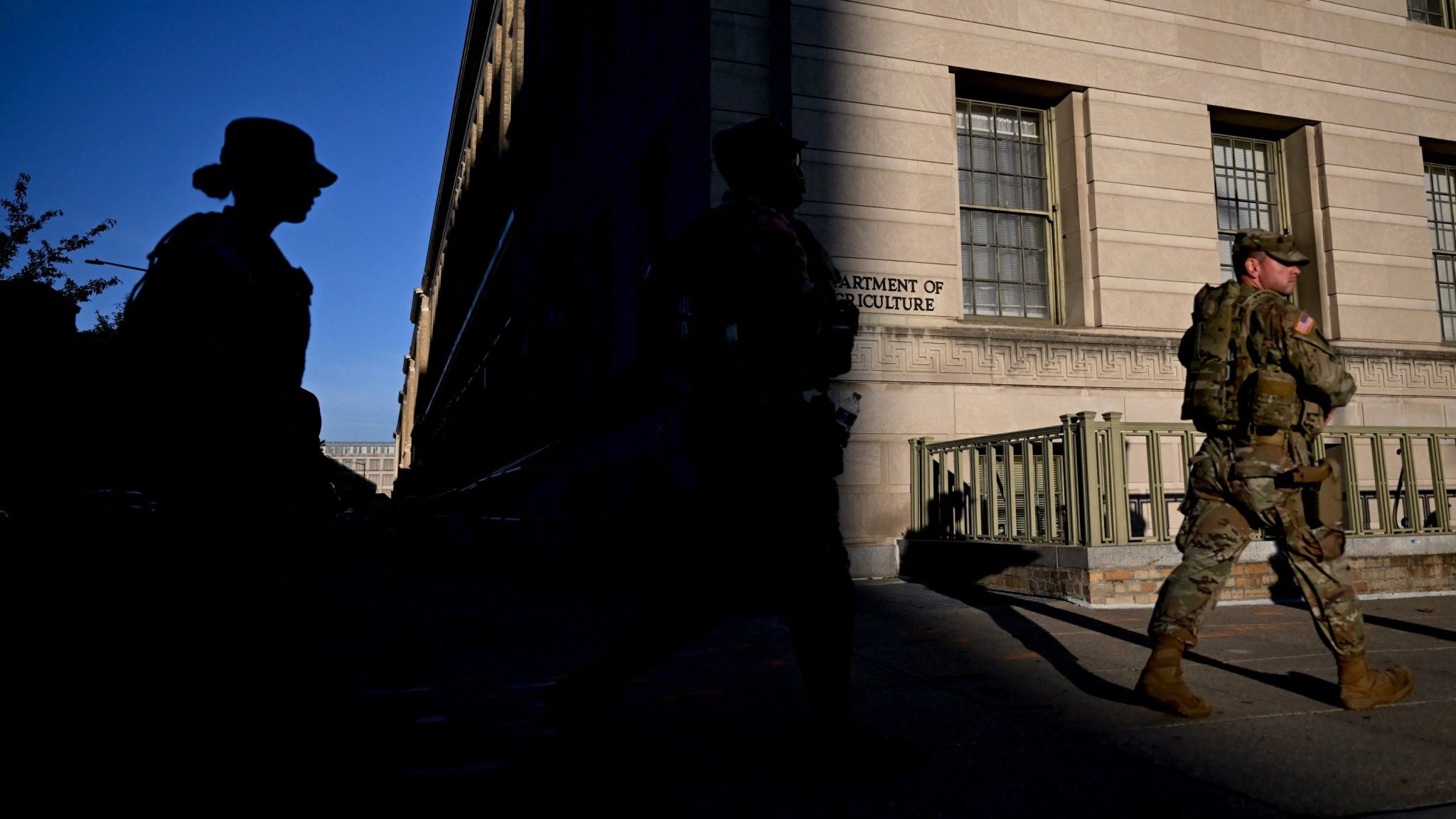 TOPSHOT - Members of the National Guard walk past the Department of Agriculture headquarters building on the seventh day of the US federal government shutdown on October 7, 2025, in Washington, DC. The US government shutdown entered its second week on October 6 with no sign of a deal between President Donald Trump's Republicans and Democrats to end the crisis. Democrats are refusing to provide the handful of votes the ruling Republicans need to reopen federal departments unless the two sides can agree on extending expiring "Obamacare" health care subsidies. (Photo by ANDREW CABALLERO-REYNOLDS / AFP) (Photo by ANDREW CABALLERO-REYNOLDS/AFP via Getty Images)