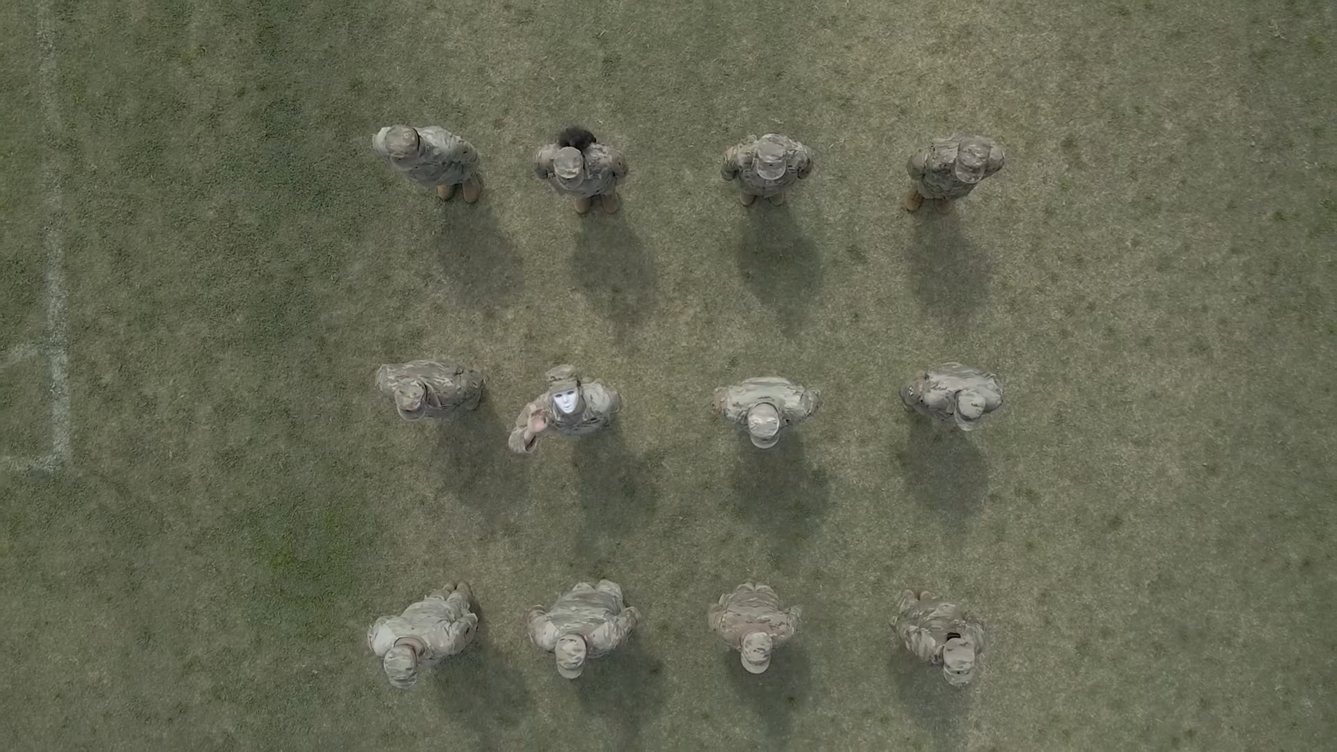 Soldiers stand in a field, one in a white mask looks up, in new PSYOP video.