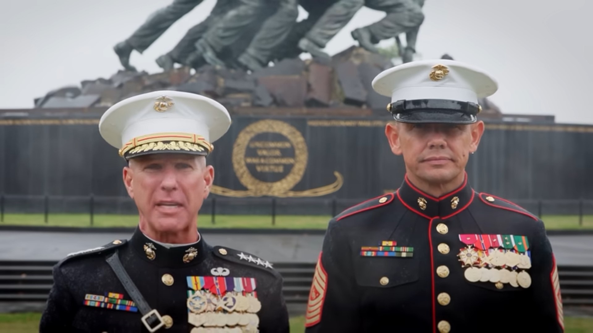 Marine Corps Commandant Gen. Eric Smith and Sgt. Maj. of the Marine Corps stand in full dress uniform next to the Marine Corps War Memorial as it rains.