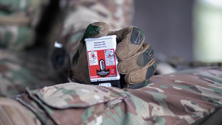 A service member practices administering the high-dose naloxone autoinjector (NAI) as a rescue treatment to counter opioid poisoning. The NAI is a pre-filled autoinjector containing 10 milligrams of the opioid antagonist naloxone and can be administered via self- or buddy-aid into the front or side of the thigh through clothing, even chemical protection gear such as Mission Oriented Protective Posture suit. Image courtesy of Kaleo.