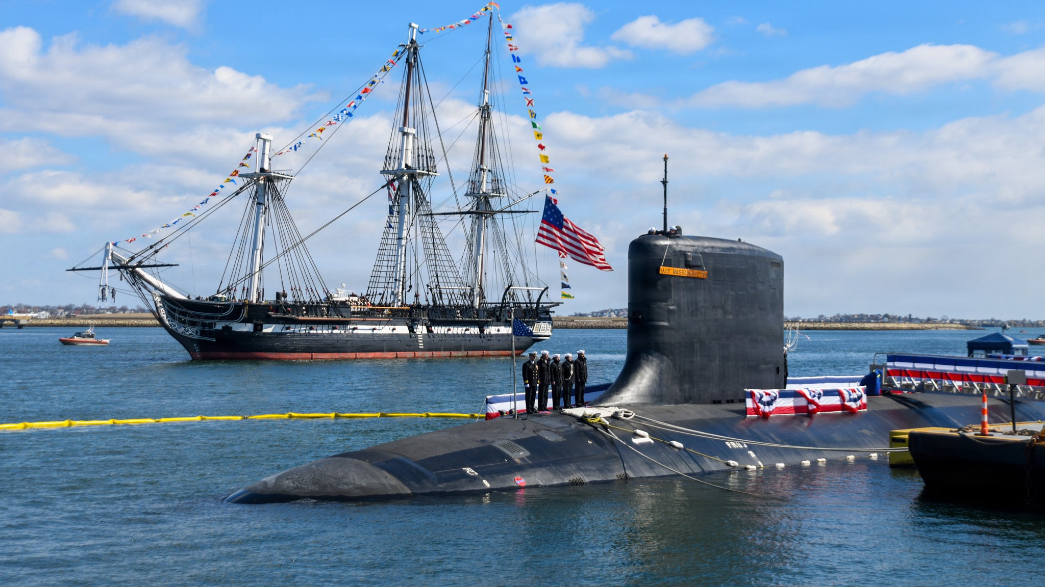 Image: The USS Constitution sails past the Virginia-class nuclear-powered fast-attack submarine USS Massachusetts (SSN 798) during Massachusetts’ commissioning in Boston, on March 28th, 2026. Massachusetts is the newest fast-attack submarine and the fifth U.S. Navy vessel to bear the name. (U.S. Navy photo by Mass Communication Specialist 2nd Class Lucas J. Hastings) 