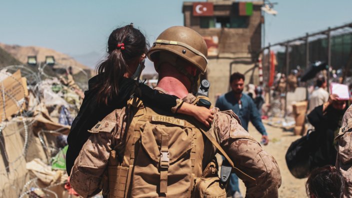 A Marine assigned to the Special Purpose Marine Air Ground Task Force-Crisis Response- Central Command carries a child to be processed during an evacuation at Hamid Karzai International Airport, Kabul, Afghanistan, Aug. 25.