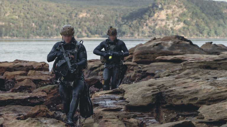 U.S. Naval Special Warfare (NSW) operators navigate over rocky terrain on the shoreline during joint over-the-beach training with Marine Raiders assigned to U.S. Marine Forces Special Operations Command as part of Exercise Talisman Sabre 25 in Sydney, Australia, July 15. Talisman Sabre is the largest bilateral military exercise between Australia and the United States, with multinational participation, advancing a free and open Indo-Pacific by strengthening relationships and interoperability among key allies and enhancing our collective capabilities to respond to a wide array of potential security concerns. NSW provides maritime special operations force capabilities to enable Joint Force lethality and survivability inside denied and contested areas. (U.S. Navy photo by Mass Communication Specialist 2nd Class David Rowe) (Portions of this image have been blurred for operational security)
