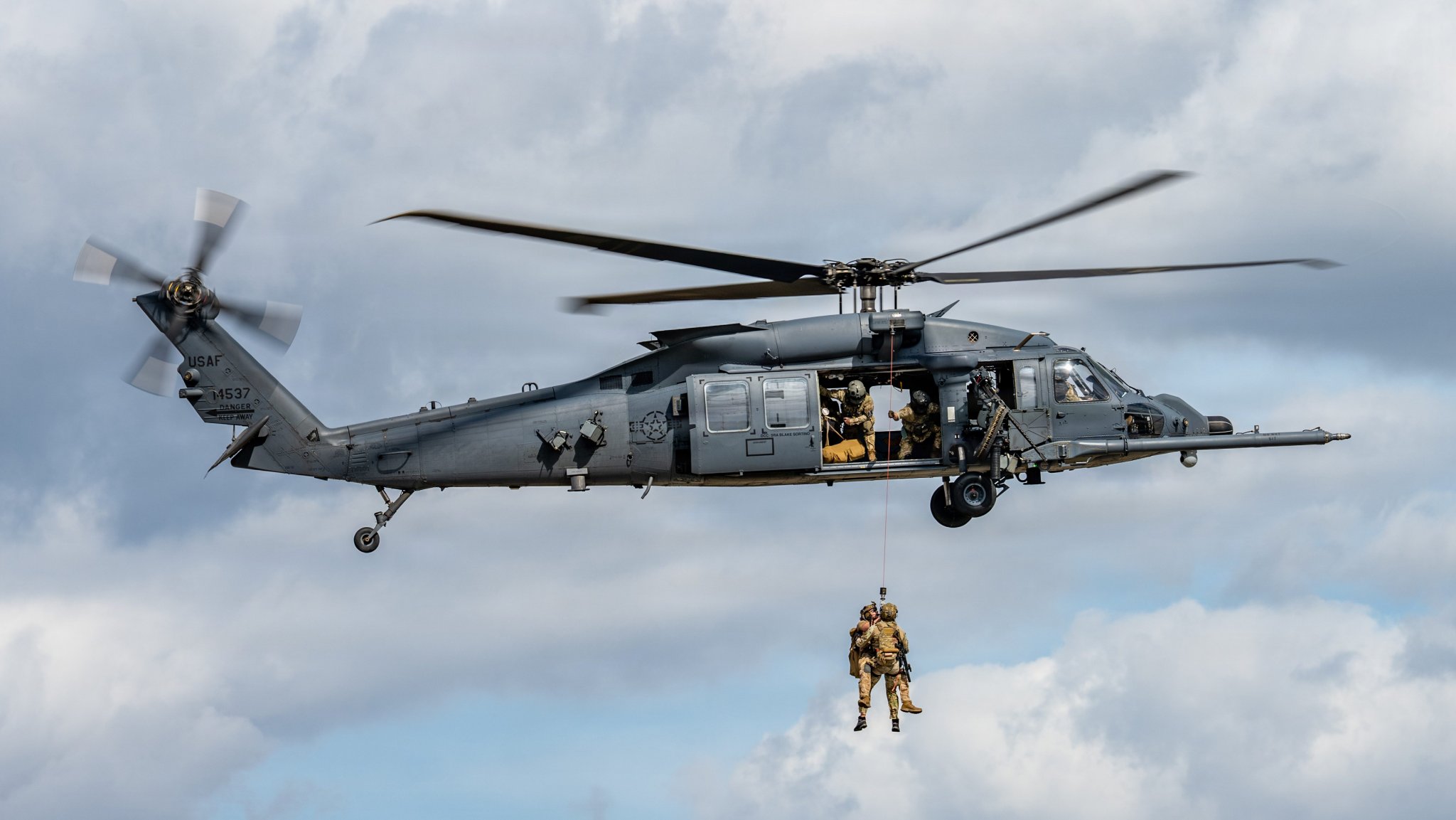 An HH-60W Jolly Green II lifts a simulated survivor into the cabin during a rescue demonstration at Moody Air Force Base, Georgia, Feb. 25, 2026. The display emphasized the aircraft’s role in combat search and rescue operations and the precision required to execute hoist procedures safely. (U.S. Air Force photo by Senior Airman Savannah Carpenter)