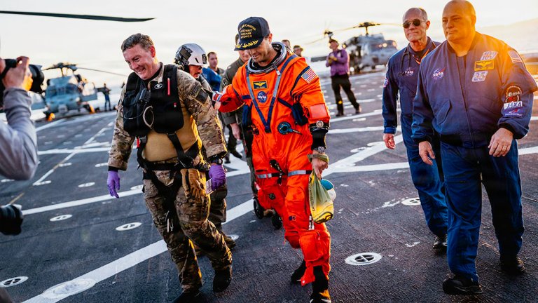 NASA astronaut Reid Wiseman walks with NASA personnel on the flight deck of the San Antonio Class amphibious transport dock USS John P. Murtha (LPD 26) after returning from space on Apr. 10, 2026. John P. Murtha is underway in the U.S. 3rd Fleet area of operations supporting NASA’s Artemis II mission, retrieving the crew and spacecraft following their return to Earth and splashdown in the Pacific Ocean. NASA’s Artemis II mission sent four astronauts on a flight around the moon in the Orion space craft, marking the first time humans journeyed to deep space in over 50 years. (U.S. Navy photo by Mass Communication Specialist 2nd Class August Clawson)