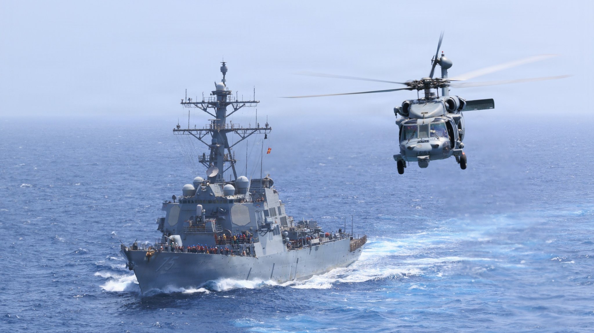 Arleigh Burke-class guided-missile destroyer USS Donald Cook (DDG 75) sails while an MH-60S Sea Hawk, attached to Helicopter Sea Combat Squadron (HSC) 5, flies alongside Nimitz-class aircraft carrier USS George H.W. Bush (CVN 77), June 18, 2026. USS George H.W. Bush is deployed to the U.S. 5th Fleet area of operations to support maritime security and stability in the Middle East. (U.S. Navy photo) 