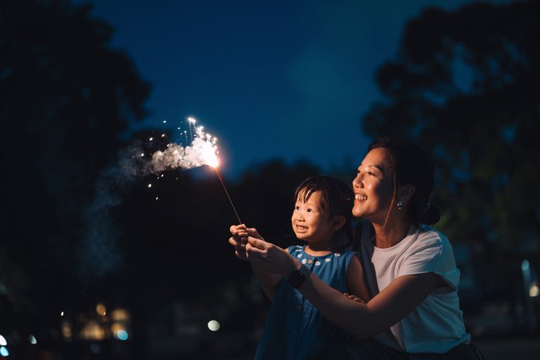 Joyful young Asian mother and little daughter having fun with fireworks in the park at night. Family enjoying a lovely moment playing with sparklers. Mother-daughter moments. Family lifestyle. Family love and togetherness