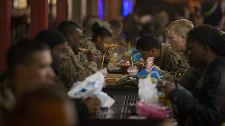 KANDAHAR, AFGHANISTAN - NOVEMBER 11: Lights from various take-aways and fast food outlets still operating illuminate diners eating at the Broadwalk at Kandahar airfield on November 11, 2014 in Kandahar, Afghanistan. Now that British combat operations have ended and the last UK base in Afghanistan had been handed over to the control of Afghan security forces, any remaining troops are leaving the country via Kandahar. As the drawdown of the US-led coalition troops heads into its final stages, many parts of Kandahar airfield - once home to tens of thousands of soldiers and contractors - are being closed or handed over to the Afghans. (Photo by Matt Cardy/Getty Images)