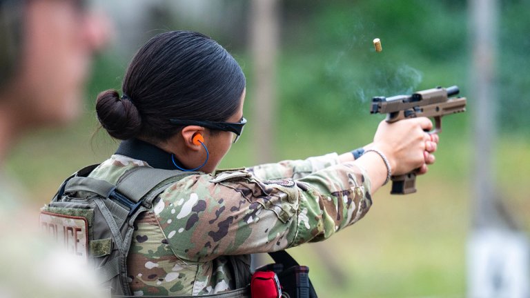 Airman Mia Marquez, 802nd Security Forces Ssquadron installation access controller, fires an M18 handgun at paper targets while U.S. Air Force Tech. Sgt. Justin Hains, 802nd Security Forces Squadron noncommissioned-officer-in-charge of training, observes the firing range while during sustainment firing training at Joint Base San Antonio-Lackland, Texas, April 9, 2024. Students participate in this training to better understand the weapons systems while also completing drills that require different firing positions to maintain proficiency and develop their firearms skills. (U.S. Air Force photo by Brian Boisvert)