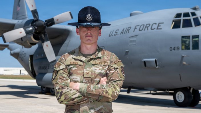 Air Force Tech. Sgt. Nathaniel Brown, 322nd Training Squadron master military training instructor, poses in front of a C-130H cargo aircraft at Kelly Field, Joint Base San Antonio-Lackland, Texas, Aug. 24, 2026. Brown, who served as a crew chief prior to his selection as a Military Training Instructor via the developmental special duty program, marshalled the C-130 crew as they parked after landing at Kelly Field.” (U.S. Air Force photo by Marcus Robins)